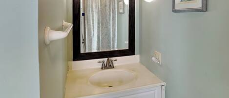A bathroom with a white sink, a mirror with a wooden frame, and a wall-mounted light fixture.