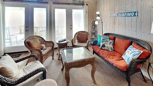 A cozy living room with wicker furniture, a glass-top coffee table, and a red sofa with tropical pillows. - Blue Shamu | Oceanfront + Screened Porch! (Topsail Beach)