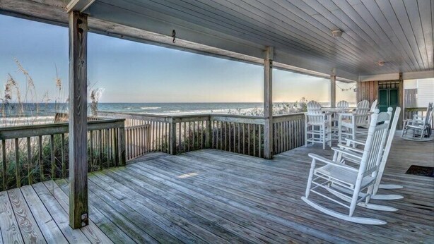 A wooden deck with white rocking chairs and tables, overlooking the ocean. - Blue Shamu | Oceanfront + Screened Porch! (Topsail Beach)