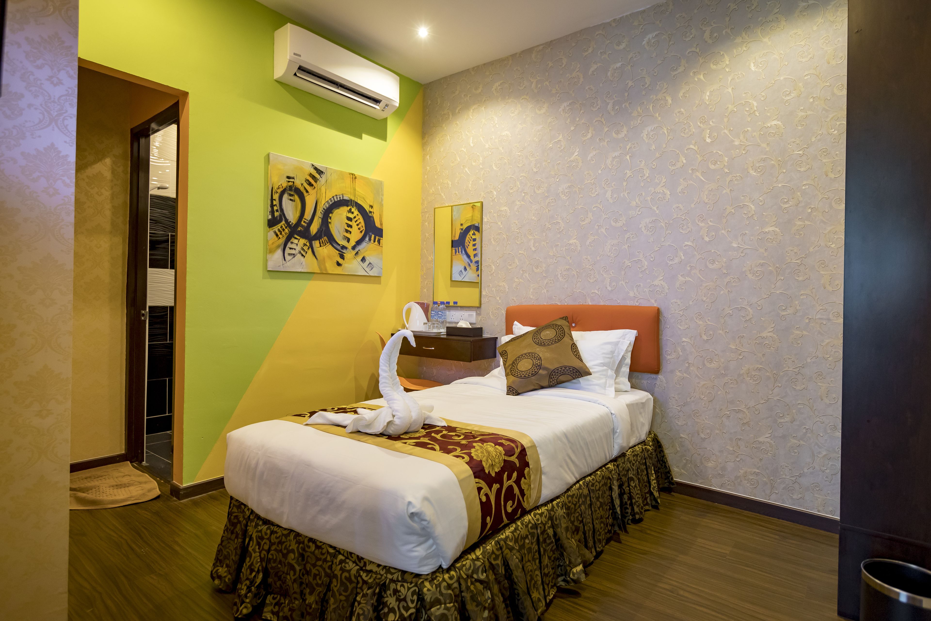 A hotel room with a neatly made bed, a bedside table with a lamp, and a wall-mounted air conditioner.