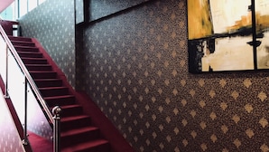 A staircase with red carpet and metal railings, leading to a room with patterned wallpaper and a large abstract painting. - Hamilton Hotel Kajang (Kajang)