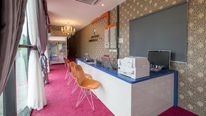 A reception desk with a computer, printer, and a mirror. There are three orange chairs in front of the desk. The room has patterned wallpaper and a chandelier. - Hamilton Hotel Kajang (Kajang)