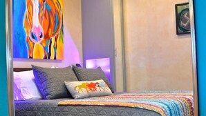 A bedroom with a wooden bed frame, a colorful horse painting, and a ceiling light fixture.