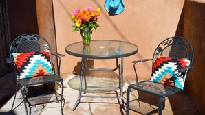 Two metal chairs with colorful geometric cushions, a glass table, and a vase with flowers.