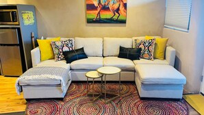 A living room with a sofa, ottoman, and coffee table, a colorful rug, and a painting of a wolf on the wall.