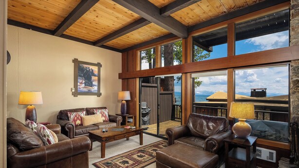 A spacious living room with leather sofas, a coffee table, and a fireplace. Large windows offer views of the outdoors. - Star Harbor # 04 by Hauserman Rentals (Tahoe City)