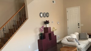 A living room with a wooden staircase, a white door, a patterned sofa, and a small wooden table. - Beautiful home in quiet neighborhood (Casa Grande)