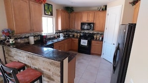 A kitchen with wooden cabinets, a granite countertop, a black refrigerator, and a window. - Beautiful home in quiet neighborhood (Casa Grande)