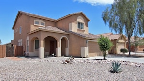 A two-story house with a tiled roof, arched entryway, and a small front yard with a tree and a cactus. - Beautiful home in quiet neighborhood (Casa Grande)