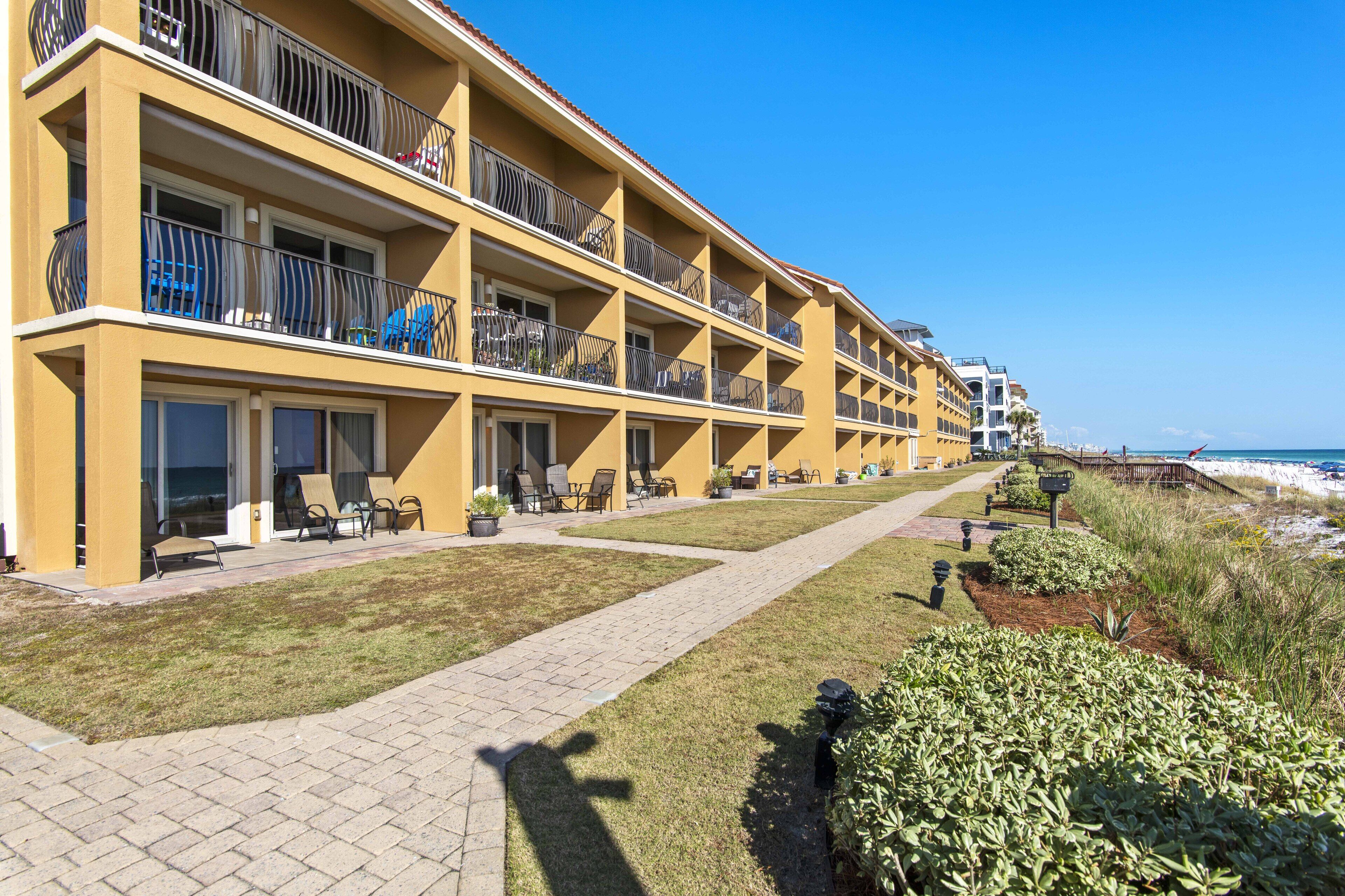 A multi-story hotel with balconies, outdoor seating, and a pathway leading to the beach.