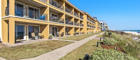 A multi-story hotel with balconies, outdoor seating, and a pathway leading to the beach.