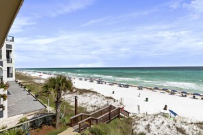 A beach view from a balcony overlooking a sandy beach with umbrellas and a clear sky.