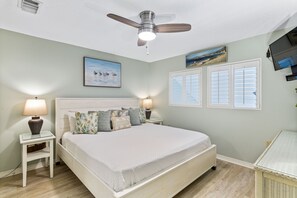 A bedroom with a bed, two bedside tables, a ceiling fan, wall-mounted TV, and artwork.