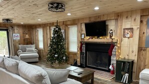 A cozy living room with a fireplace, a Christmas tree, and a television. - Autumn Ridge Cottages (Lexington)
