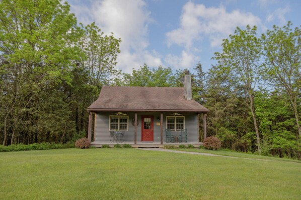 A single-story house with a red front door, a chimney, and a small porch with two chairs. - Autumn Ridge Cottages (Lexington)