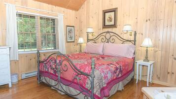 A bedroom with a wooden paneled wall, a metal bed frame, a pink bedspread, two bedside lamps, and a window with a curtain.