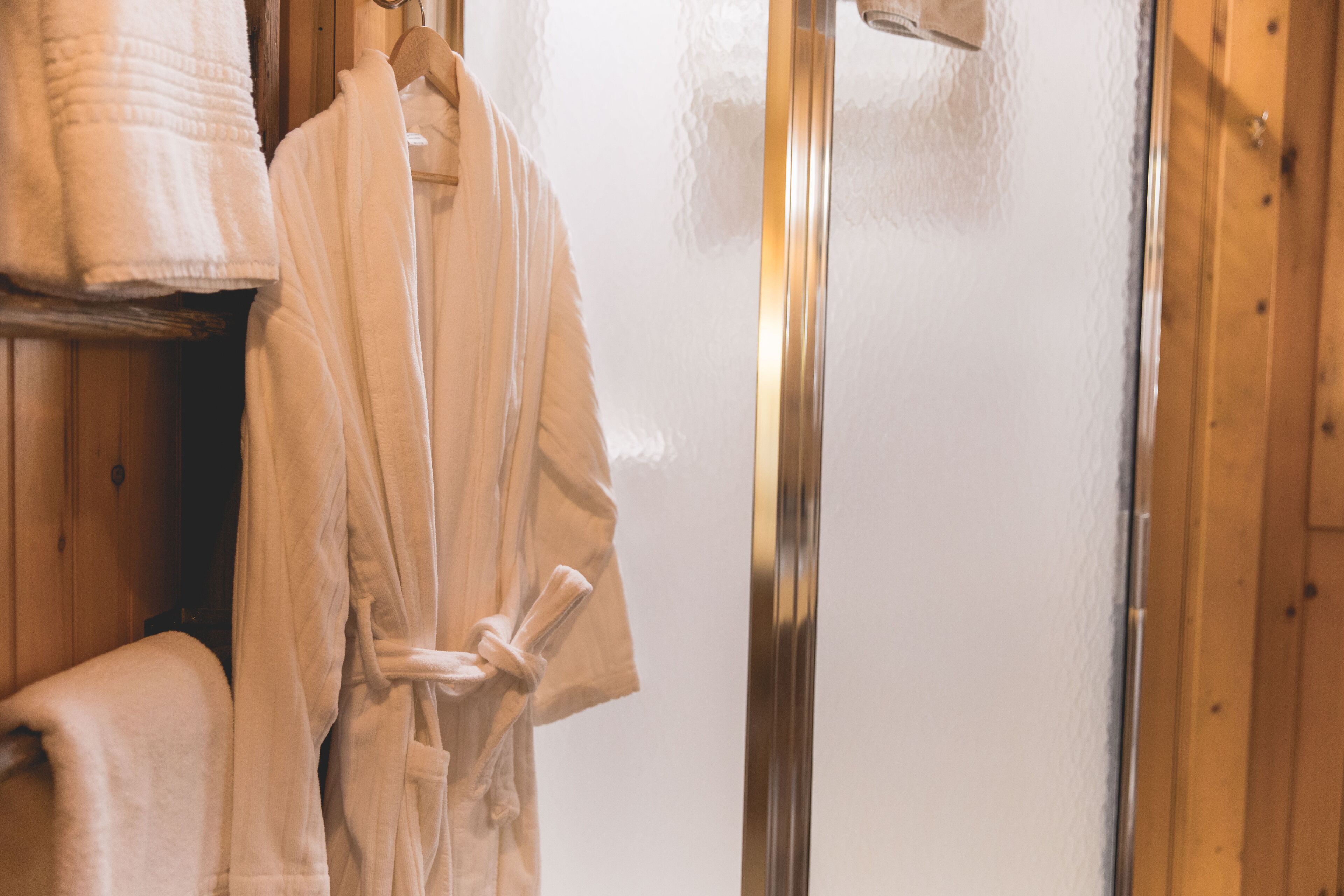 Un baño con paredes de madera, puerta de ducha de vidrio y toallero con una toalla blanca y una bata.