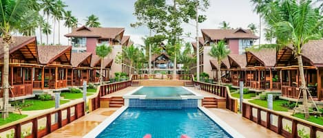Un resort con piscina central, un tobogán rojo y varias cabañas rodeadas de palmeras.