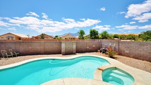 Piscina com design curvo, cercada por um muro de tijolos e uma pequena área de jardim com churrasqueira.