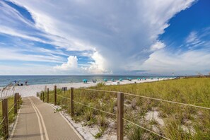 Ein Strandweg führt zu einem Sandstrand mit Sonnenschirmen und einem Holzsteg.