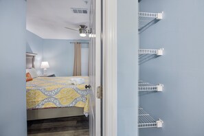 Une chambre à coucher comprenant un lit, une table de chevet, une lampe, une fenêtre avec des rideaux et un ventilateur de plafond.