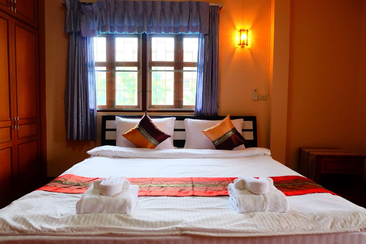 A neatly made bed with white linens, decorative pillows, and a red decorative item.