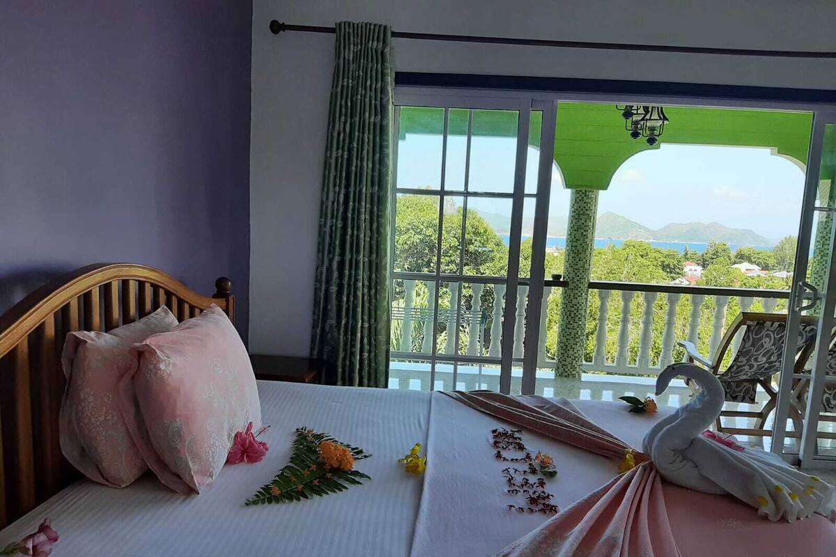 A bedroom with a bed, pillows, a decorative swan, and a balcony with a view.