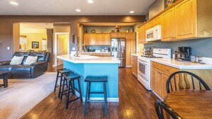A modern kitchen with wooden cabinets, a central island, and a dining area with a wooden table and chairs. - West Sail - Play & Work in Hood River! River & Mountain Views, Quiet, Walk to Downtown (Hood River)