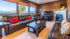 A living room with a leather sofa, a coffee table, a fireplace, and a television. - West Sail - Play & Work in Hood River! River & Mountain Views, Quiet, Walk to Downtown (Hood River)