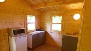 A compact wooden cabin with a kitchenette, including a refrigerator, microwave, sink, and cabinets.