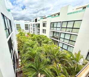 Un hotel de varios pisos con balcones, un patio central con palmeras y un cielo despejado.