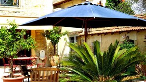 An outdoor patio area with a table and chairs, a large umbrella, and potted plants. - Le Clos des Aramons (Bernis)