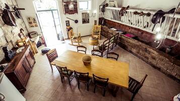 A rustic dining area with a wooden table and chairs, surrounded by stone walls and a white fence with hanging items.
