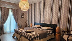 A bedroom with a large bed, striped curtains, a hanging light fixture, and a wooden floor. - Le Clos des Aramons (Bernis)
