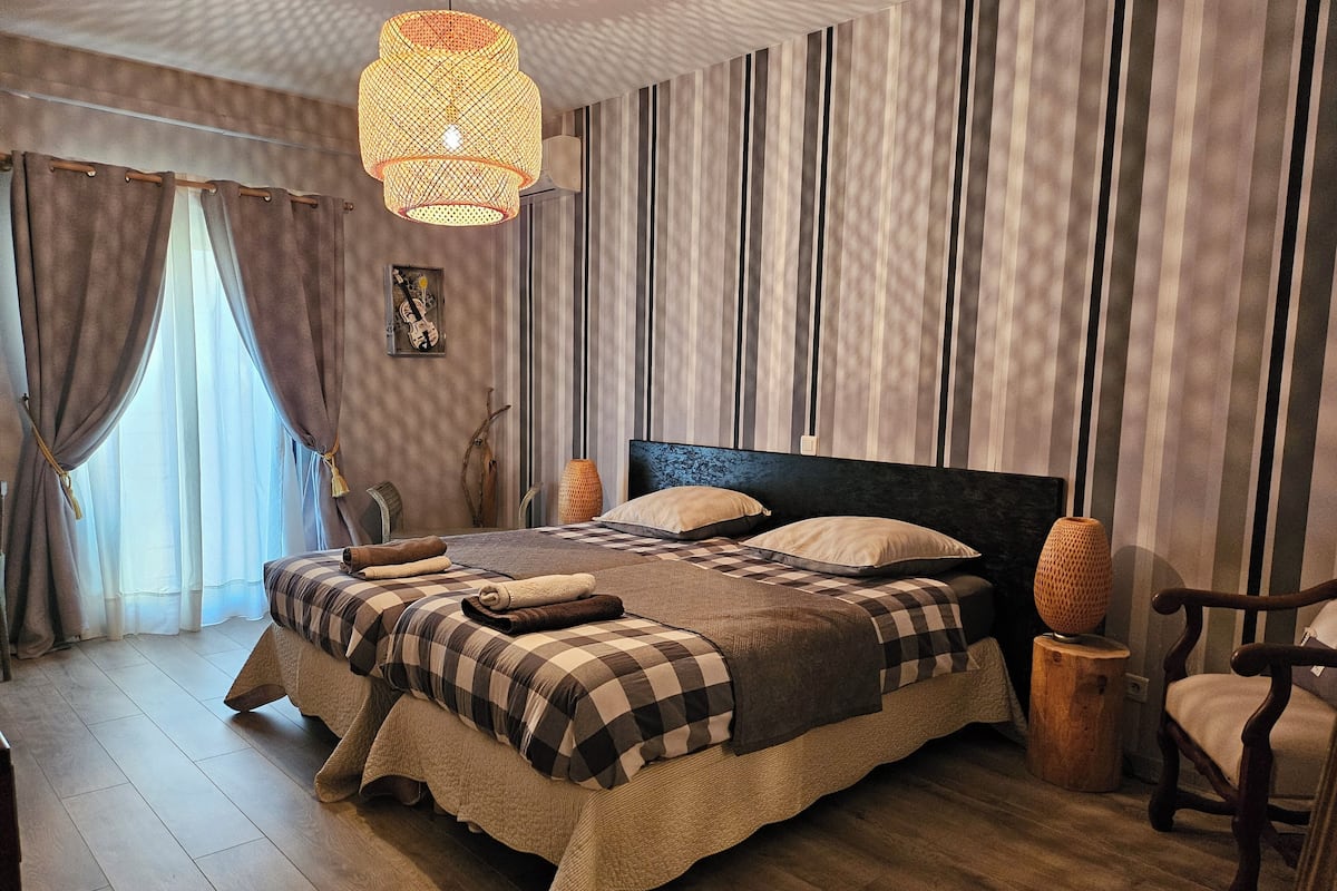 A bedroom with a large bed, striped curtains, a hanging light fixture, and a wooden floor.
