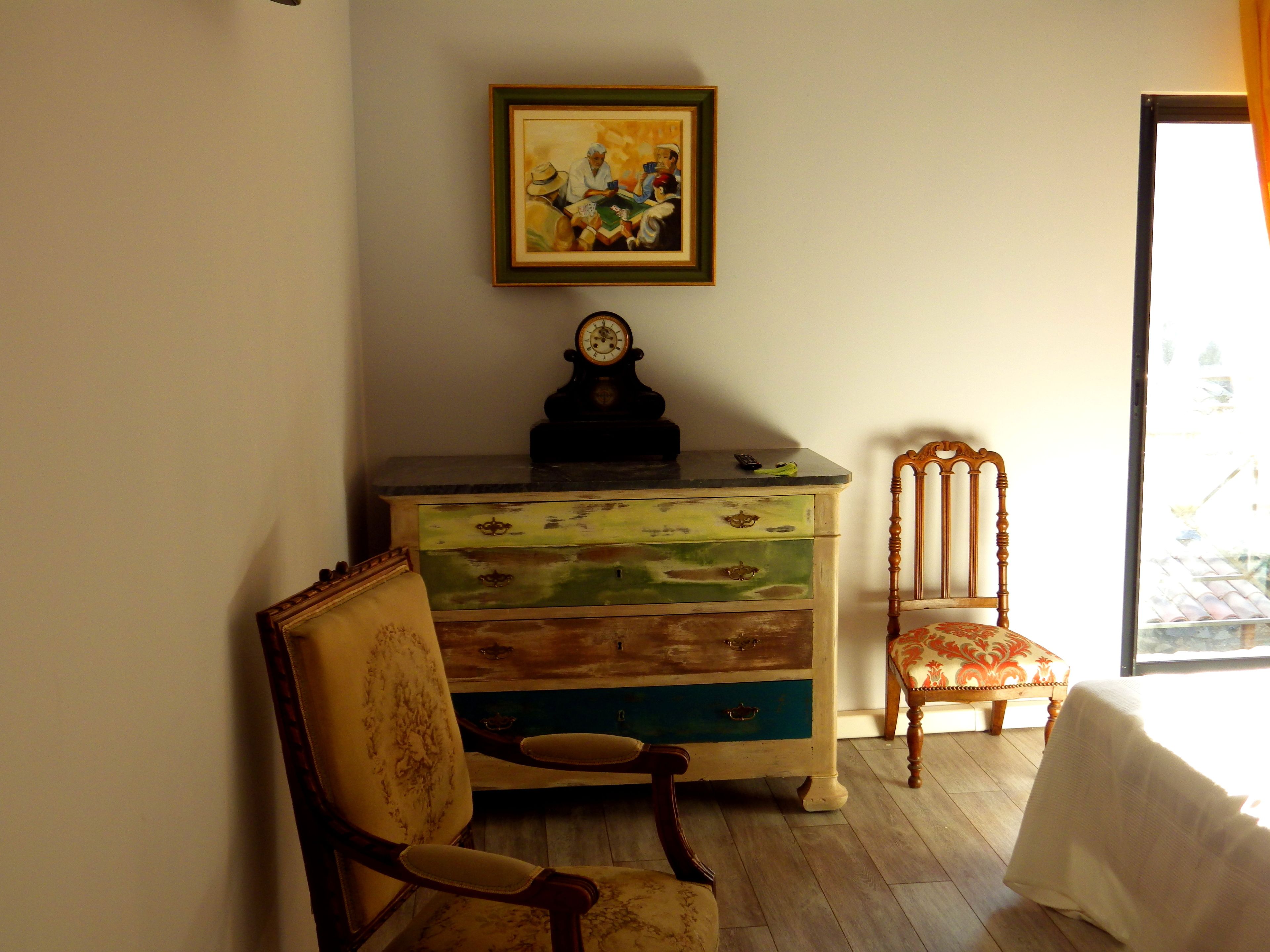 A room with a wooden dresser, a chair, and a framed painting on the wall.