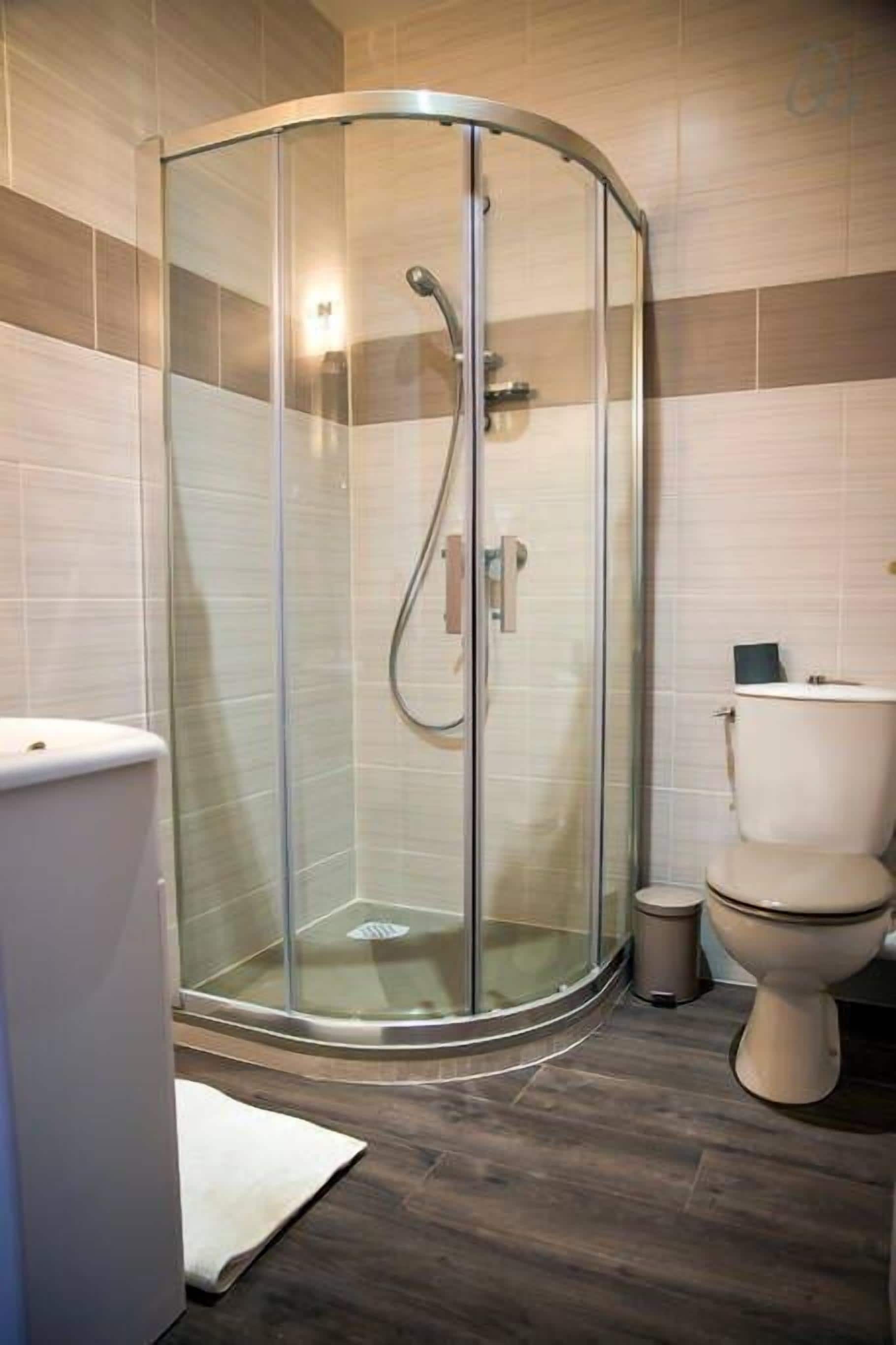 Un bagno moderno con doccia vetrata, un water e un cestino.