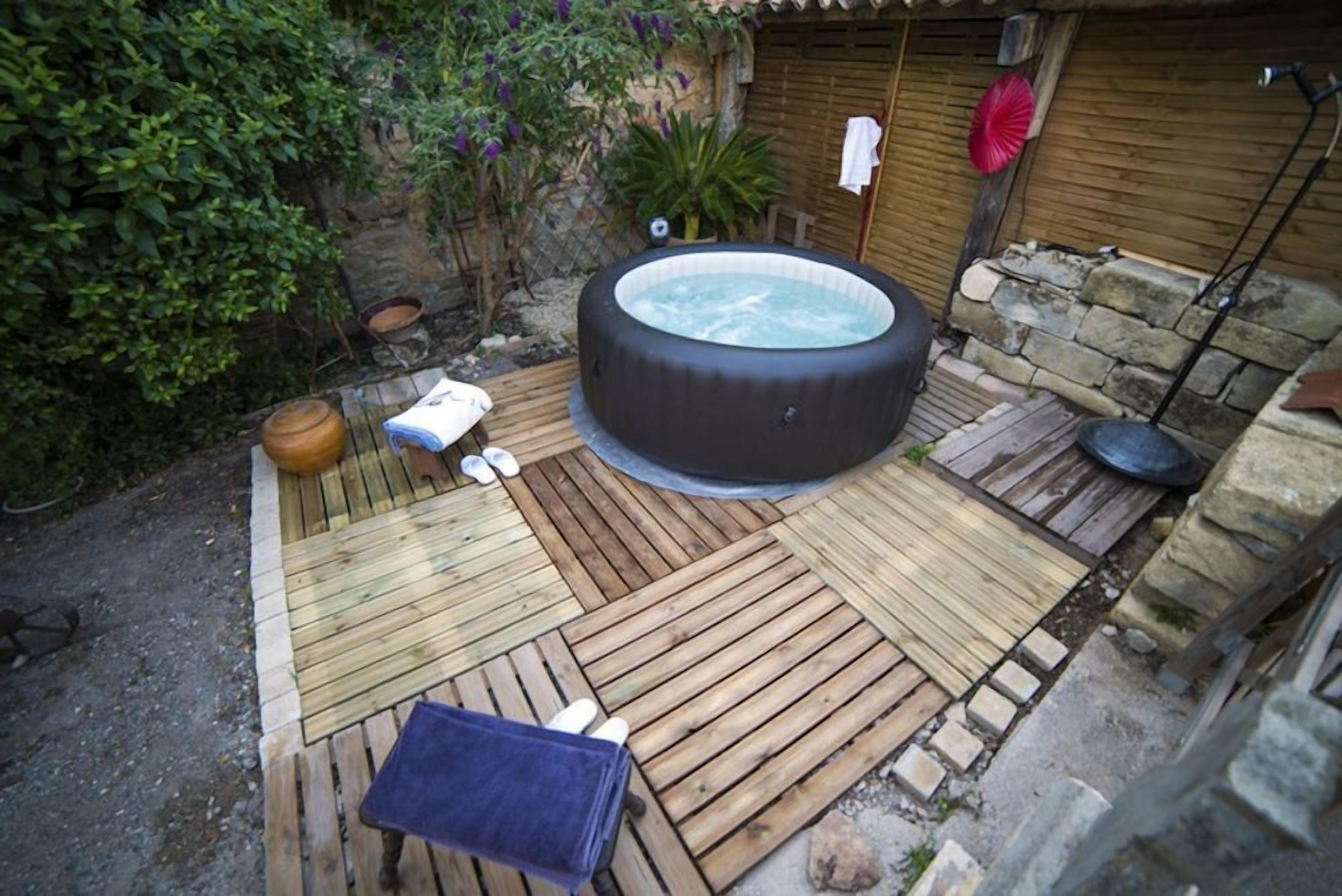 A hot tub surrounded by wooden decking, a stone wall, and a small table with a towel.
