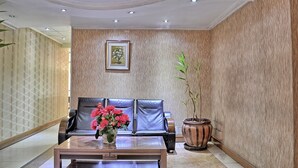 Un hall d’entrée avec un canapé en cuir, une table basse ornée d’un vase de fleurs, une plante en pot et un tableau encadré au mur.