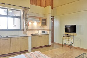 A compact kitchen with wooden cabinets, a microwave, and a TV on a stand. - Space International (Nairobi)