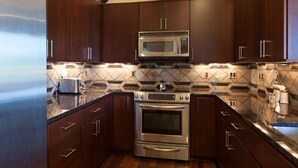 Cozinha moderna com armários de madeira escura, eletrodomésticos de aço inoxidável e painel de fundo com padrão.