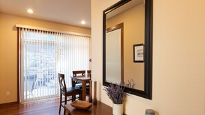 Uma área de jantar com uma mesa de madeira, cadeiras e um banco. Há uma janela com persianas, um vaso com flores e um quadro na parede.