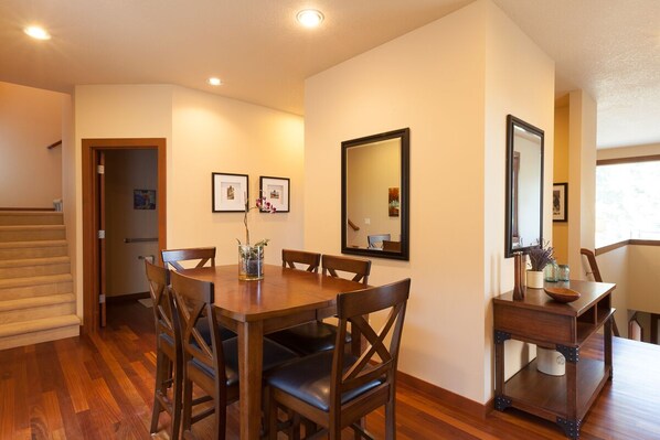 Un coin repas avec une table et des chaises en bois, une petite table d’appoint sur laquelle est posé un vase, et des tableaux encadrés accrochés au mur.