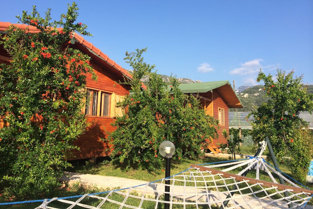 A wooden cabin with a red roof, surrounded by lush greenery and red flowers.