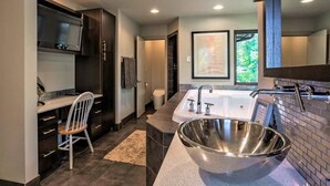 Un baño moderno con una bañera independiente grande, muebles de color oscuro y un pequeño escritorio con una silla.
