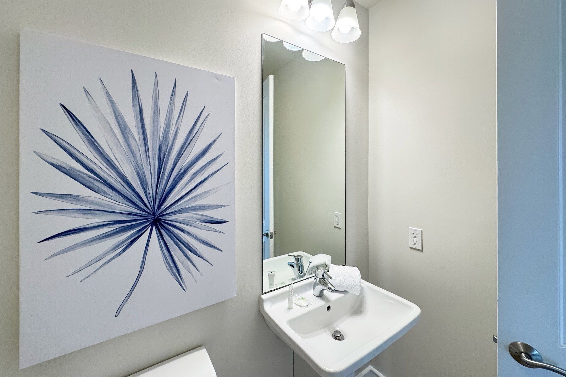Uma casa de banho com uma pia branca, um espelho e um quadro abstrato azul na parede.
