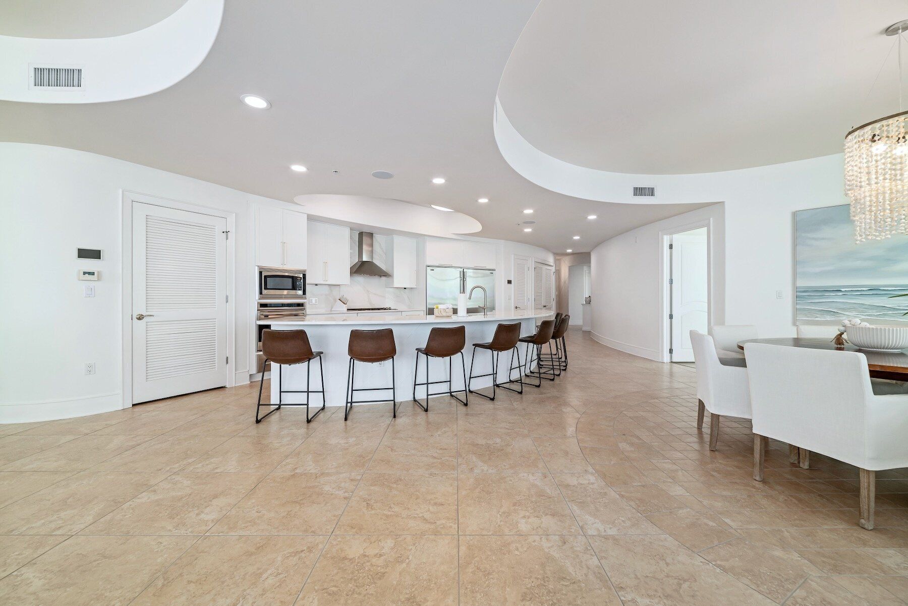 A modern kitchen with a central island, bar stools, and a dining area with a view of the ocean.