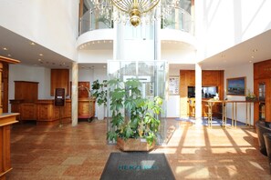 A spacious lobby with a central plant display, a reception desk, and a view of the upper floor. - Hotel Poinger Hof (Poing)