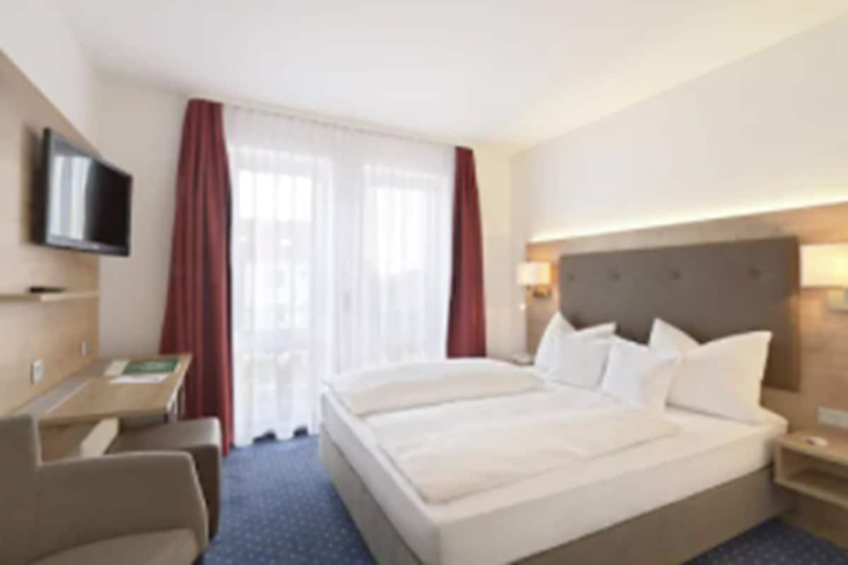 A hotel room with a large bed, a desk, a chair, a flat-screen TV, and a window with curtains.