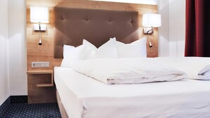 Hotellihuone, jossa on suuri sänky, puinen pääty, yöpöytälamput ja yöpöytä.